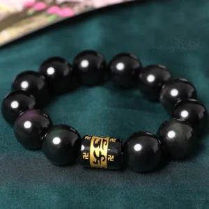 Rainbow obsidian Om Mani Padme Hum Buddhist bracelet with golden mantra bead - top view on dark fabric
