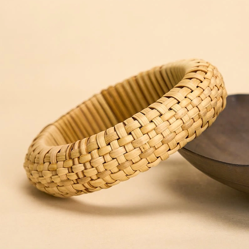 Natural rattan bangle bracelet showing detailed woven texture and warm tan tone, side angle tabletop display