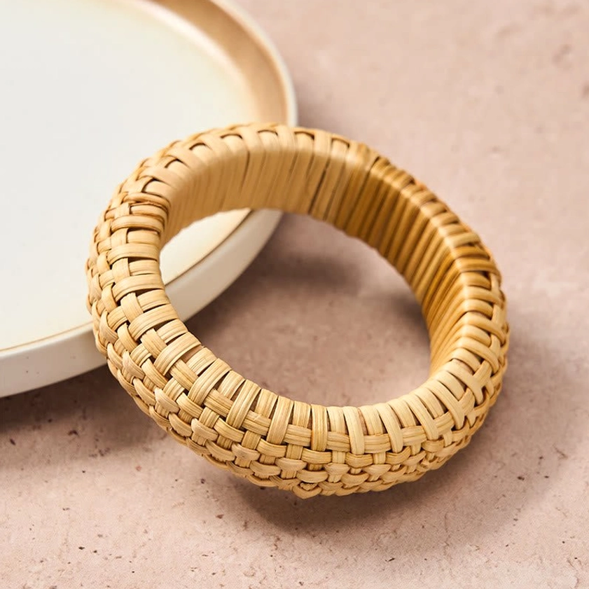 Hand-woven rattan grounding bangle with light beige tight weave, front oblique view on ceramic tableware background