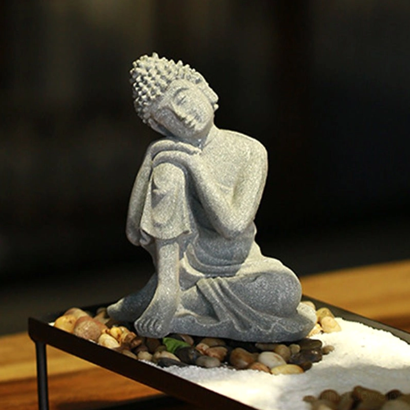 Resting Buddha decoration with relaxed reclining pose on zen pebble tray, grey stone texture and left three-quarter view