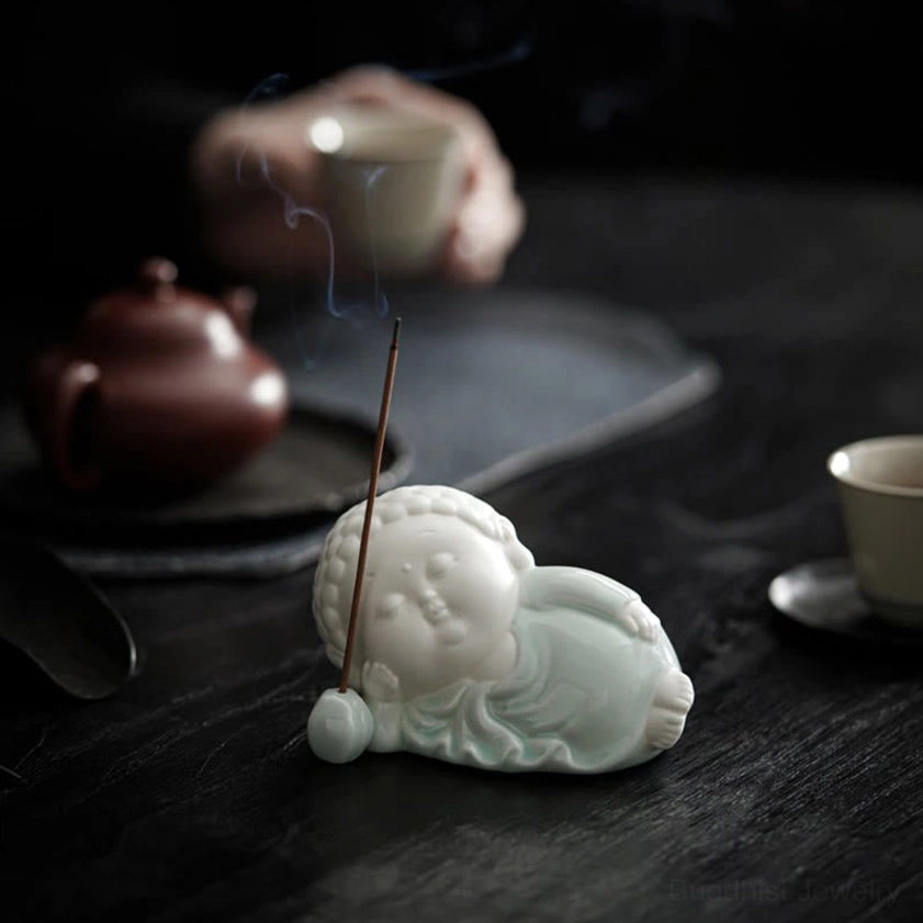 Reclining Buddha incense burner with lit incense stick displayed on traditional tea table - eye-level desktop meditation setup