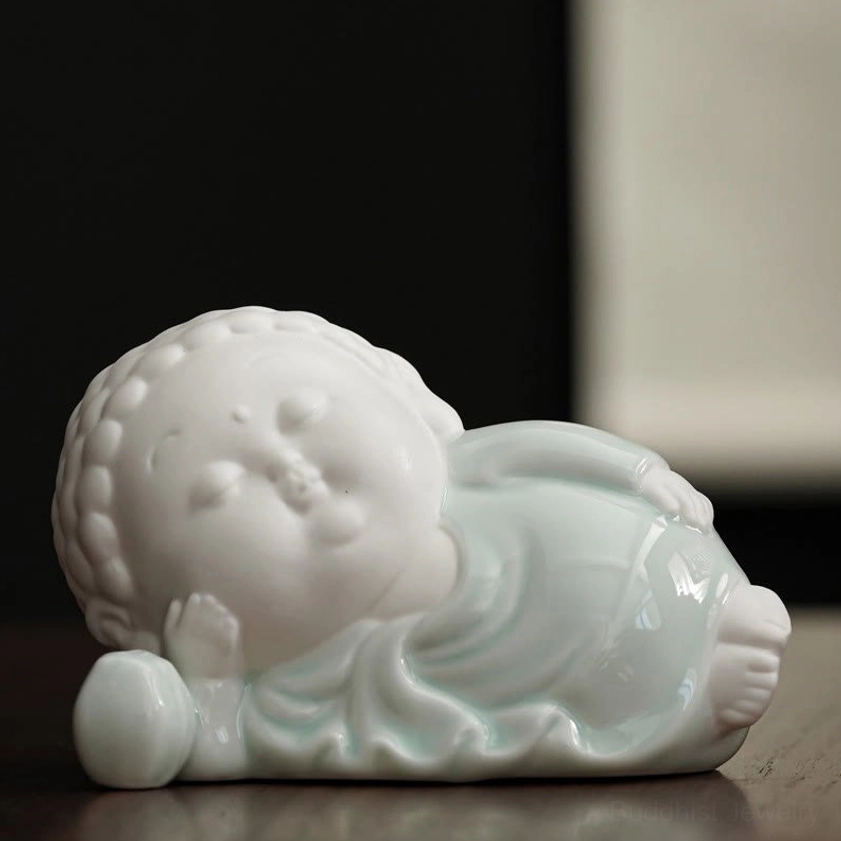 Reclining Buddha ceramic figure lying on side with hand resting on head - parinirvana peace pose on wooden desk