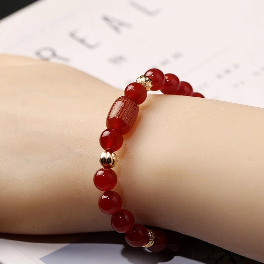 Red agate Buddhist bracelet with large sutra bead worn on human wrist, lifestyle view against book background