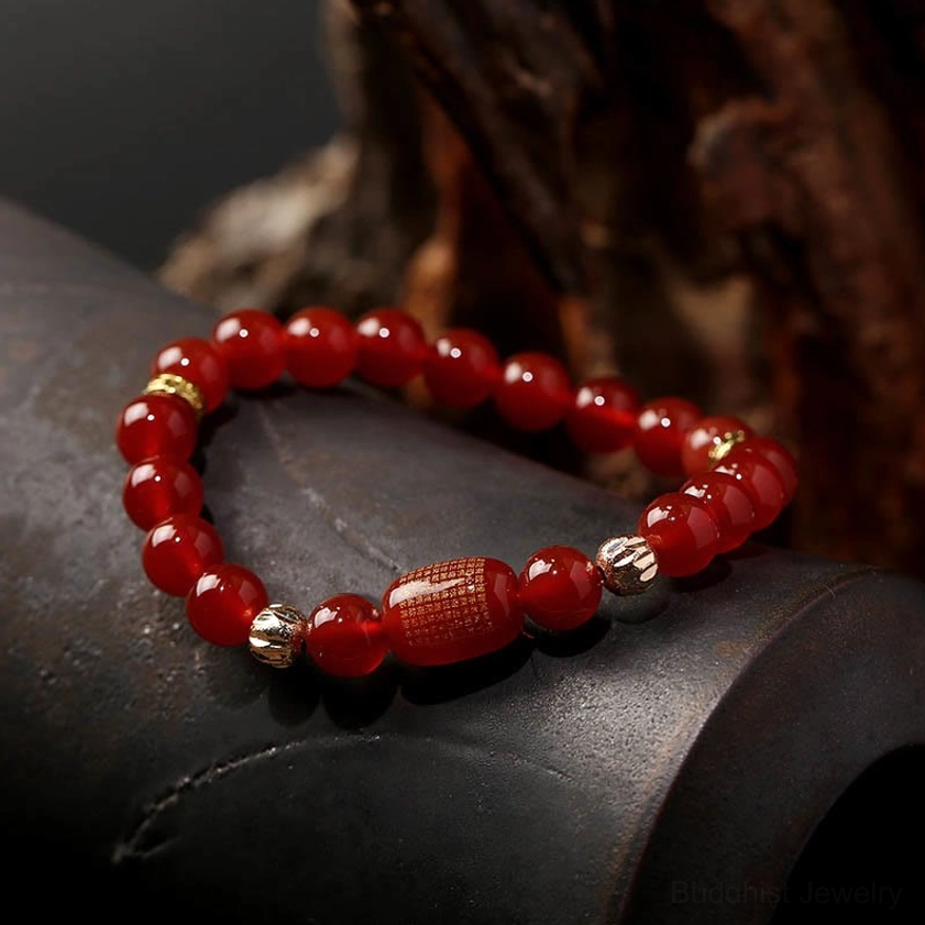 Red agate Buddhist sutra bracelet with round red beads, large red engraved barrel bead and metal spacers on wooden background