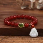 Red agate Buddha bracelet with polished beads and white jade Buddha pendant on wooden surface with dried botanicals, showcasing authentic natural stone handmade craftsmanship