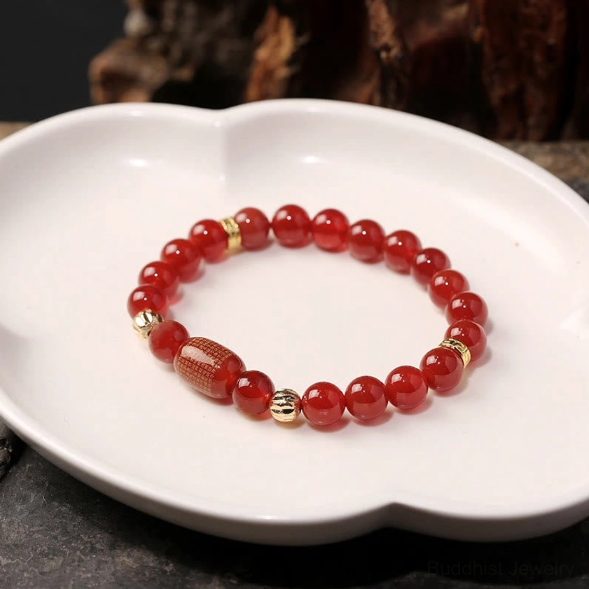 Natural red agate beads with engraved red barrel bead and gold spacers on white ceramic plate with wooden backdrop