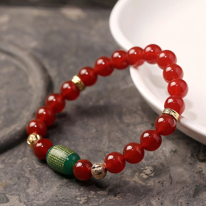 Natural red agate bracelet with green engraved sutra bead and metal spacers on marble surface, flat lay photography