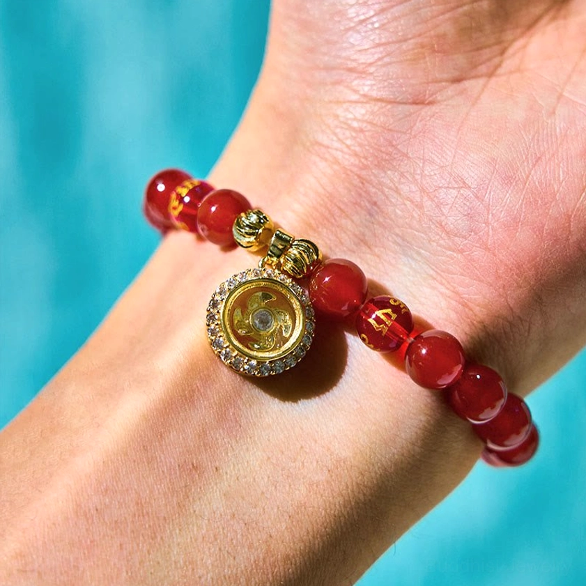 Woman wearing red agate Buddhist bracelet with engraved cyclone gold charm on wrist