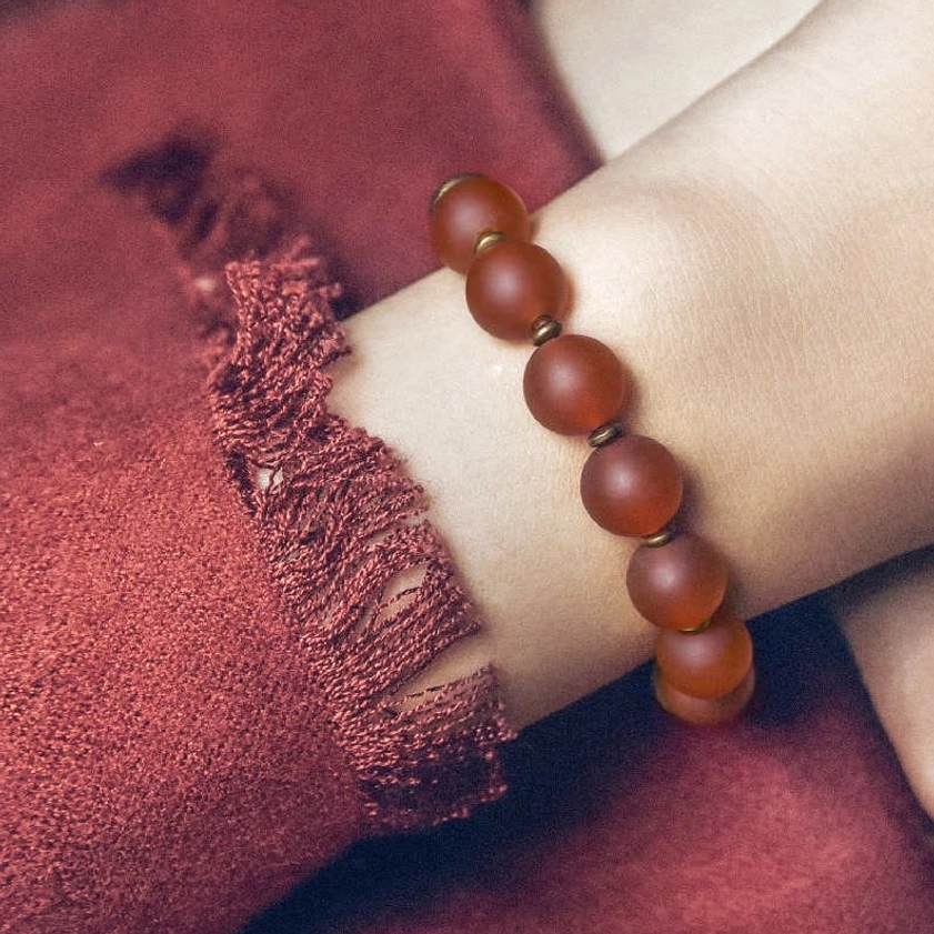 Red agate Buddhist bracelet worn on wrist with matte reddish-brown beads and bronze details