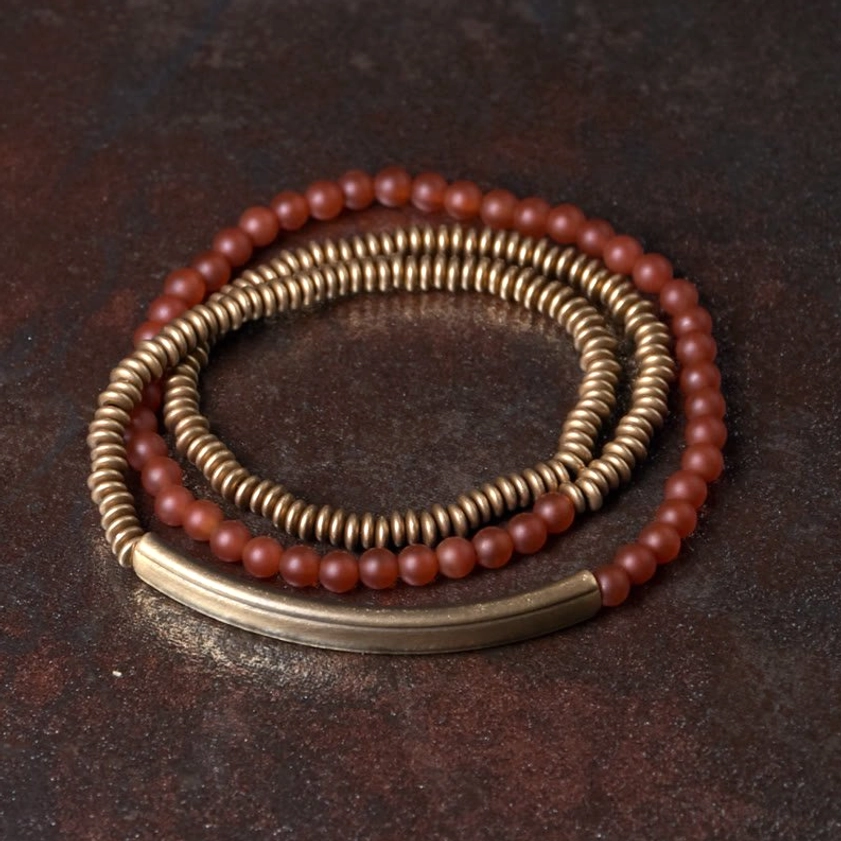 Red agate copper triple wrap Buddhist bracelet flat lay top-down view on dark wooden surface showing stacked wrap design with brass spacer accents