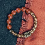 Red agate copper Buddhist bracelet with hammered bronze spacer beads, flat lay view on dual-tone fabric
