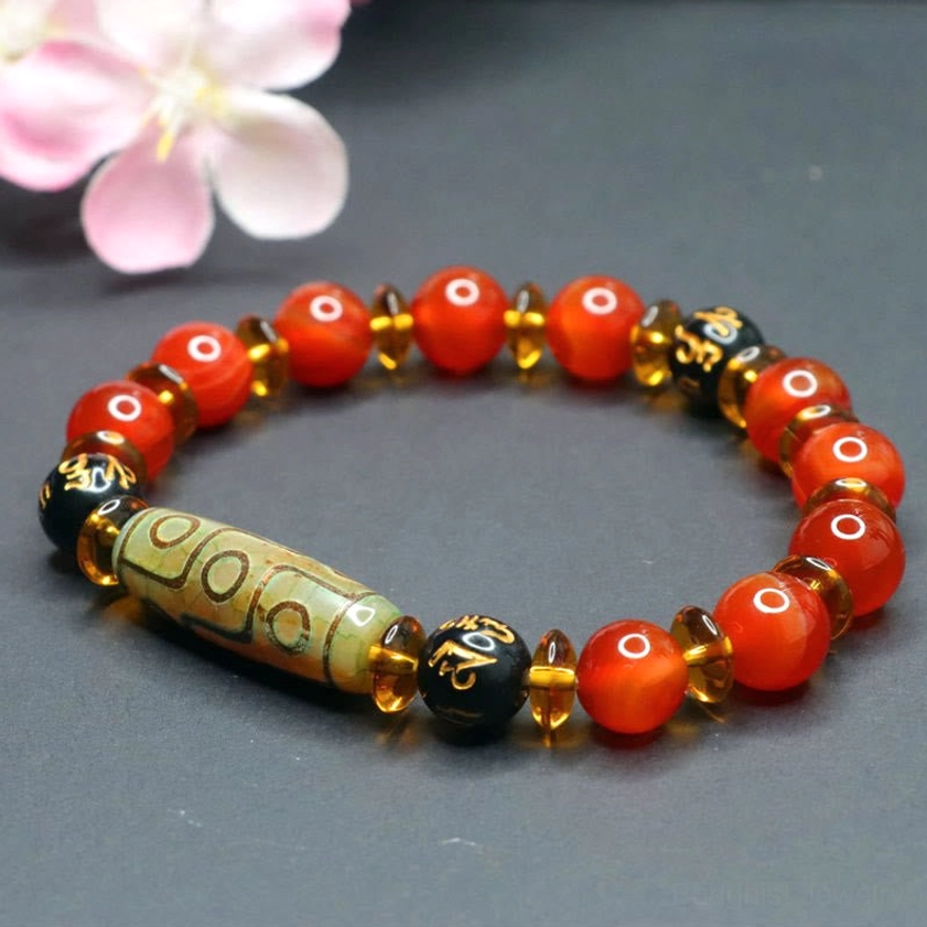 Nine-eye dzi bead Buddhist bracelet with red agate stones and gold spacers - angled view with pink cherry blossoms