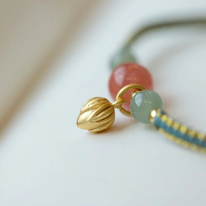 Red agate bracelet detail close-up showing gold bud charm and jade beads