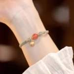 Red agate lotus bracelet with gold bud charm worn on wrist in daily feminine outfit