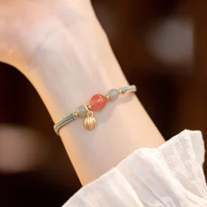 Red agate lotus bracelet with gold bud charm worn on wrist in daily feminine outfit
