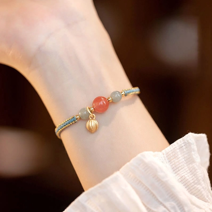 Red agate lotus bracelet with gold bud charm worn on wrist in daily feminine outfit