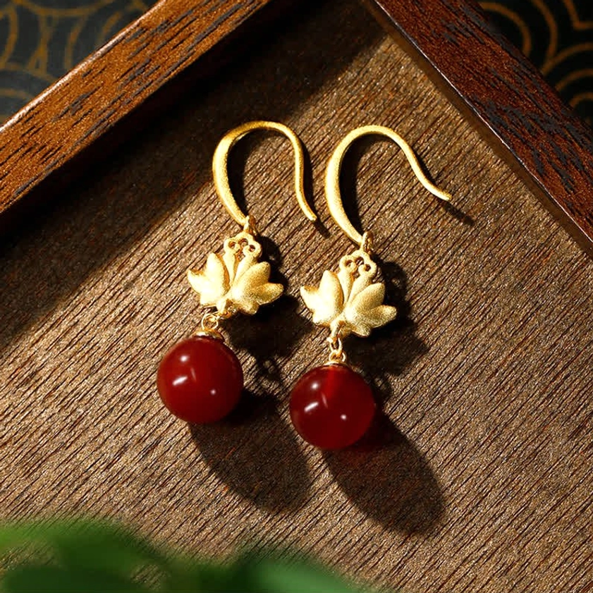 Close-up detail of red agate lotus drop earrings with matte gold lotus charm, solid stone pendants, and hypoallergenic ear hooks