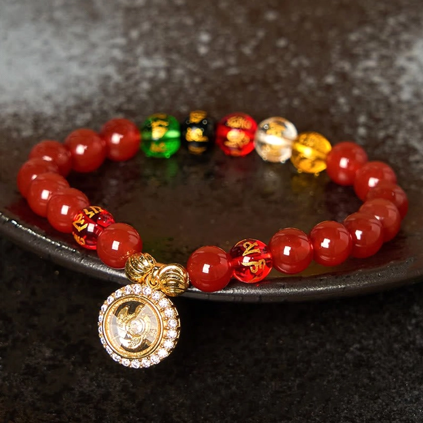 Red agate om mani padme hum bracelet with diamond-encrusted gold charm on black ceramic plate