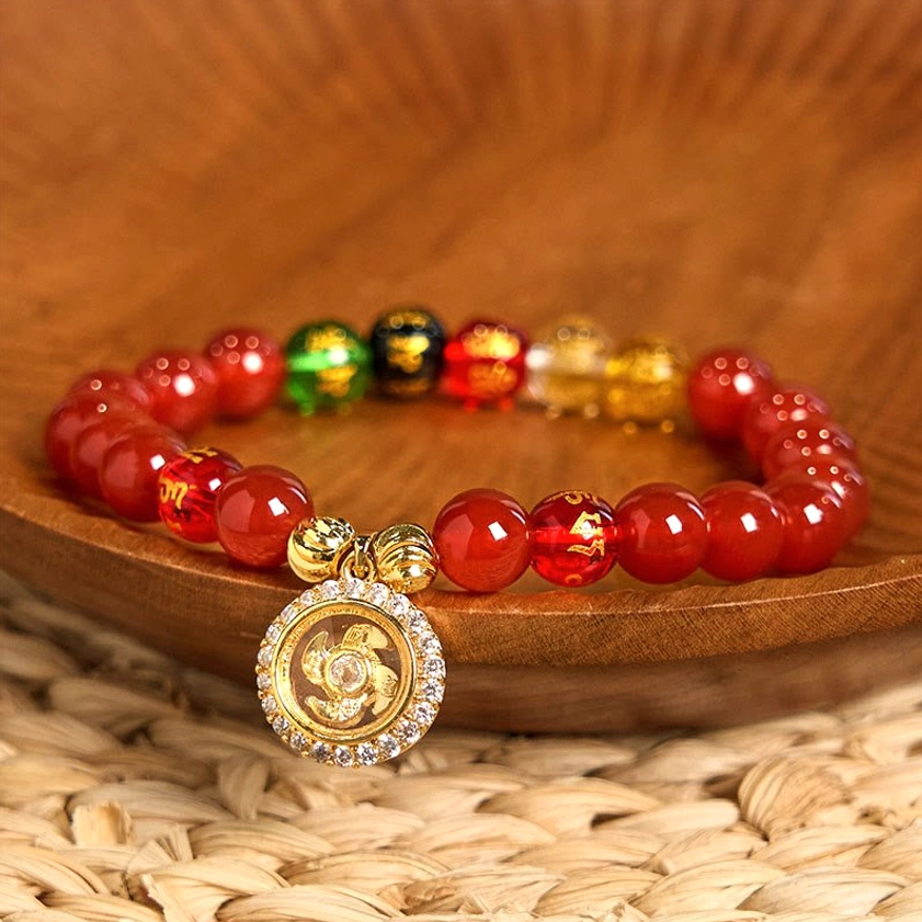 Red agate om mani padme hum Buddhist bracelet with 18K gold-plated cyclone charm on wooden display