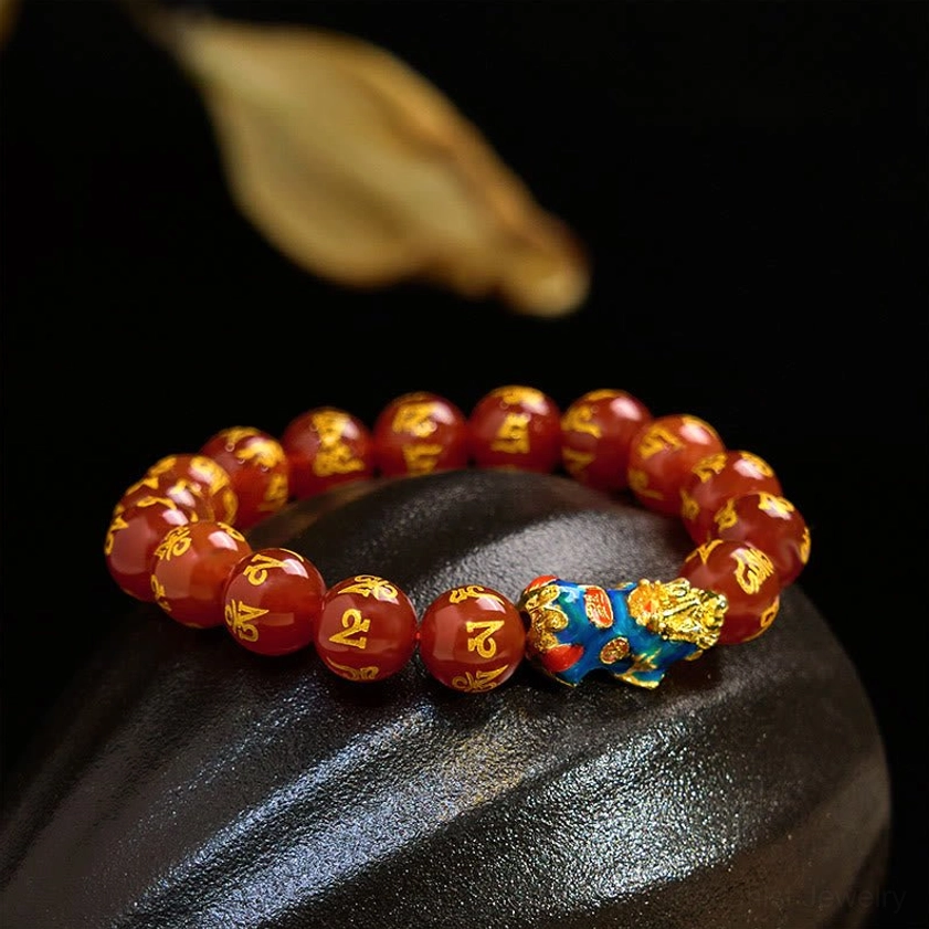 Flat lay top-down shot of red agate Pixiu mantra bracelet on dark polished stone, showing glossy polished beads with gold engravings and central Pixiu ornament