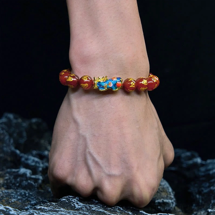 Red agate Pixiu bracelet worn on wrist against dark rock background, demonstrating fit on adult wrist, red beads with gold mantra markings