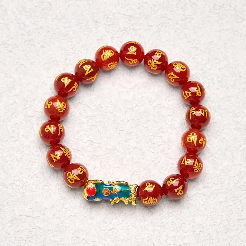 Top-down flat view of red agate Pixiu Om Mani Padme Hum bracelet on light gray background, round polished beads with gold Sanskrit script and blue-gold Pixiu charm