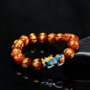 Red agate Pixiu Buddhist bracelet with Om Mani Padme Hum mantra beads, top-down view on polished black surface, gold Sanskrit text details with blue-gold color-changing Pixiu charm