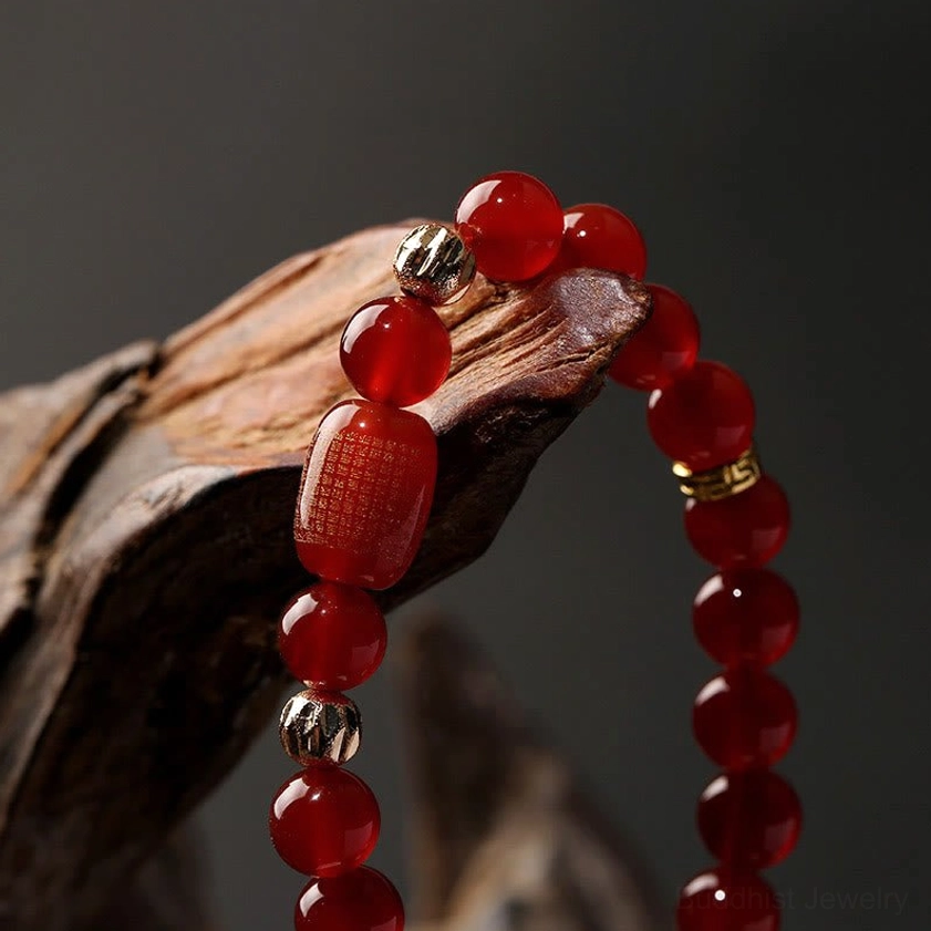 Red agate bracelet with large engraved sutra bead and round beads, side close-up view on wooden decorative prop