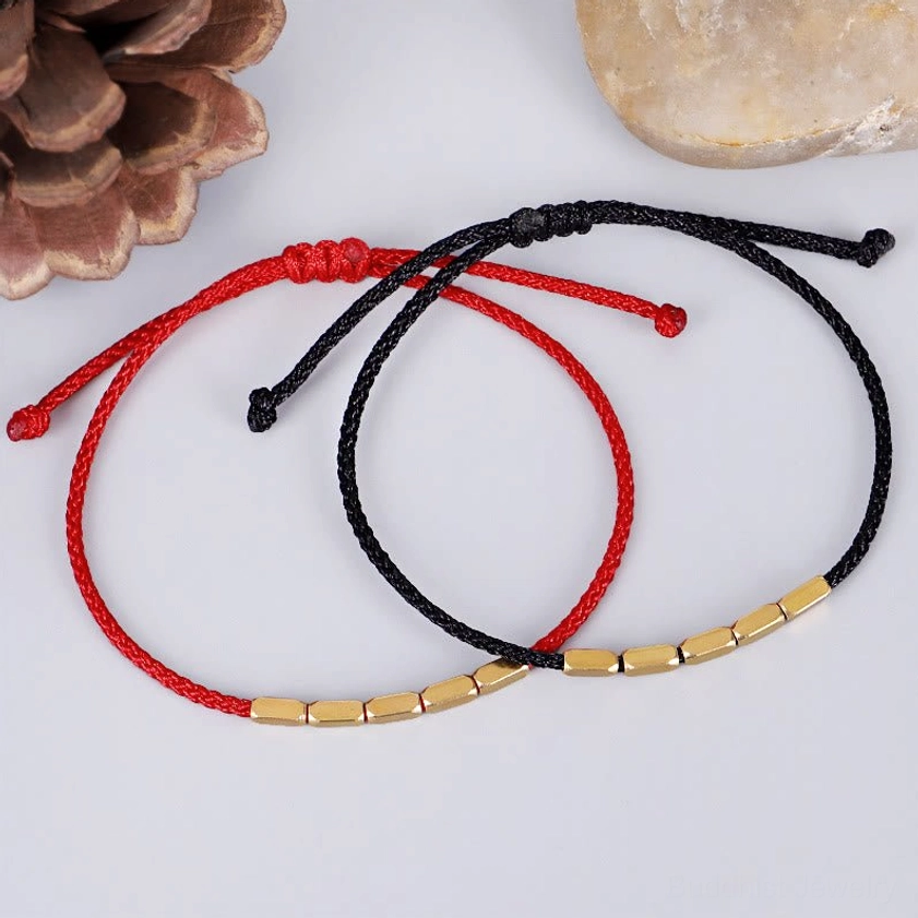 Red and black Buddhist string bracelets with copper beads displayed together on natural stone background, showing color options