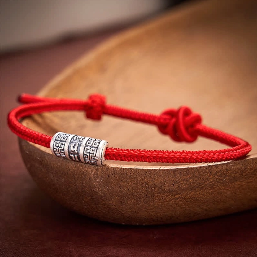 Braided red cord Buddhist protection bracelet with silver mantra bead on wooden surface, close-up product photography