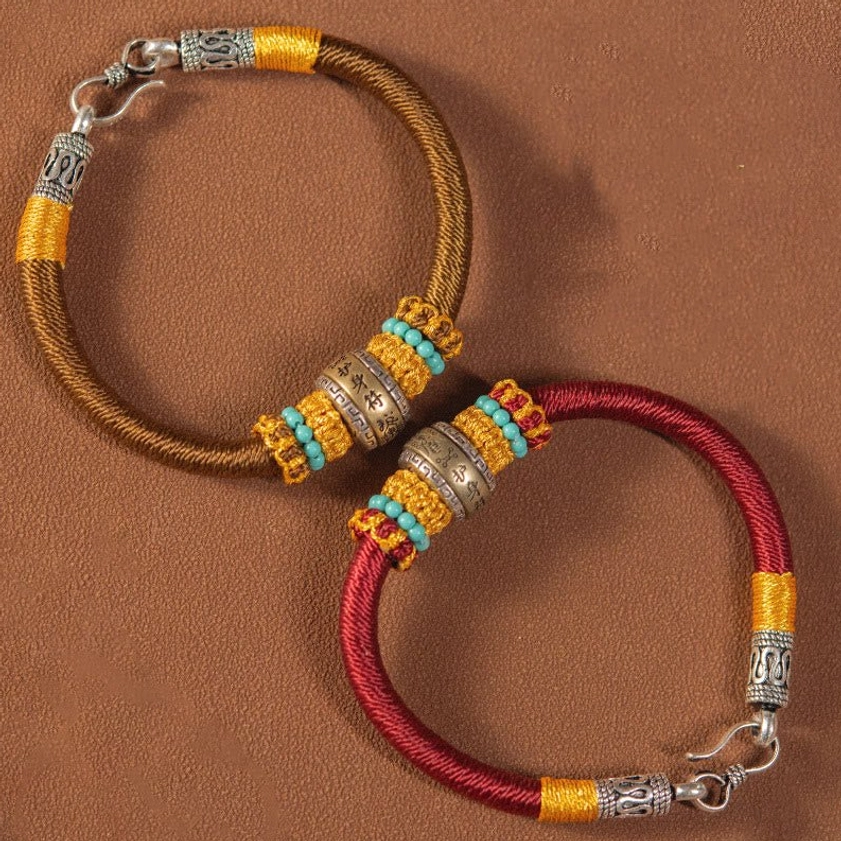 Two Buddhist protection bracelets - red and brown woven cord variants with vintage silver hardware and beaded details displayed together
