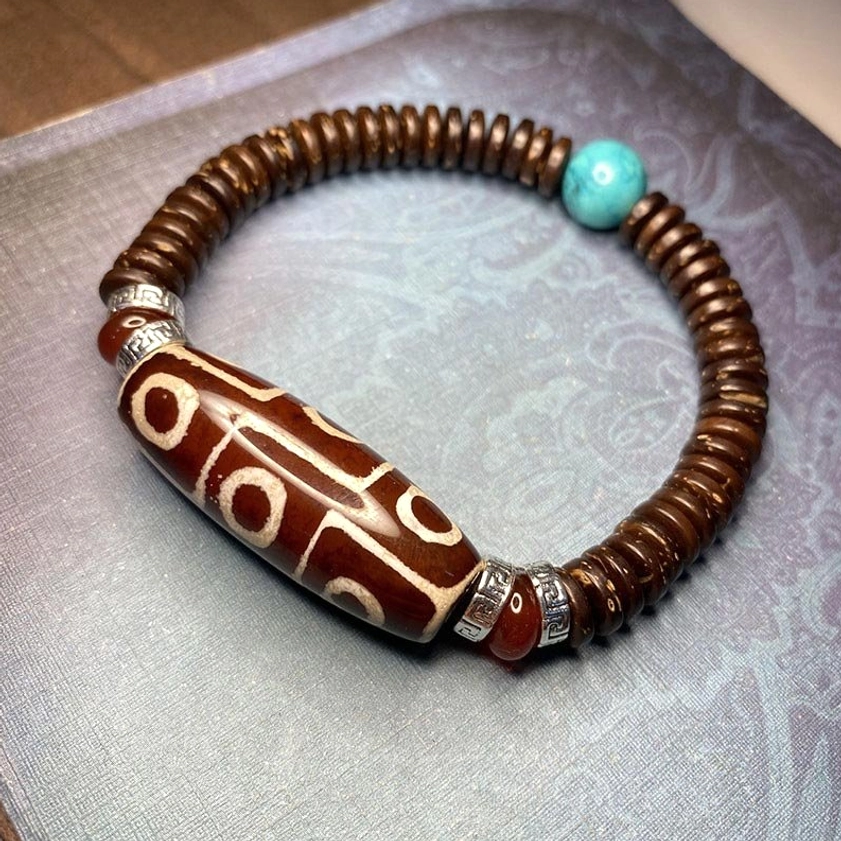red-brown nine-eye dzi bead bracelet with bold white eye patterns, coconut shell beads, and turquoise and silver accents