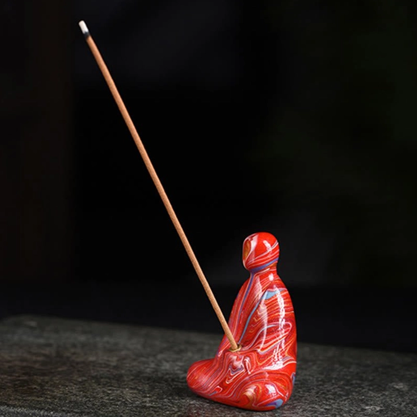 Red marbled Buddha incense holder with incense stick inserted in torso socket, side three-quarter view