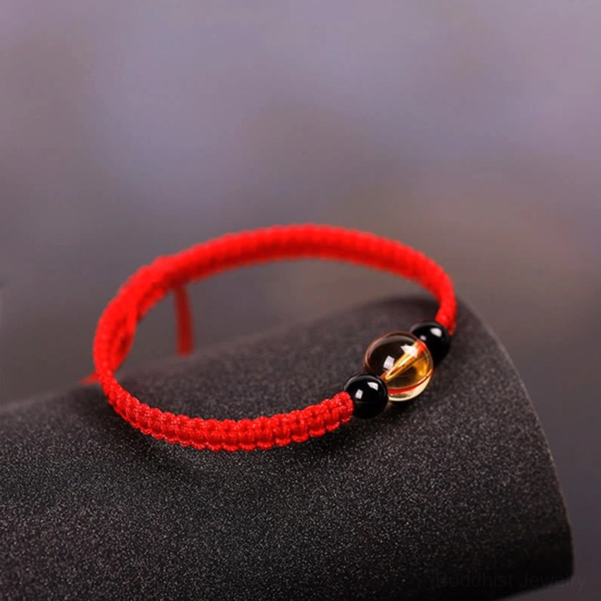 Red string bracelet with citrine and black obsidian beads on black velvet fabric background