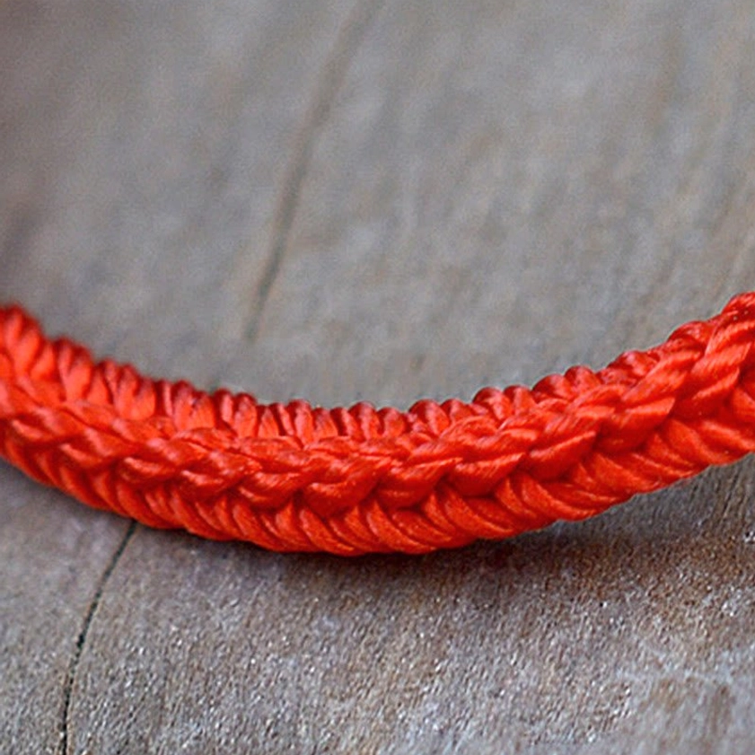 Detailed side view of solid red eight-thread Buddhist braided bracelet showing neat woven rope texture