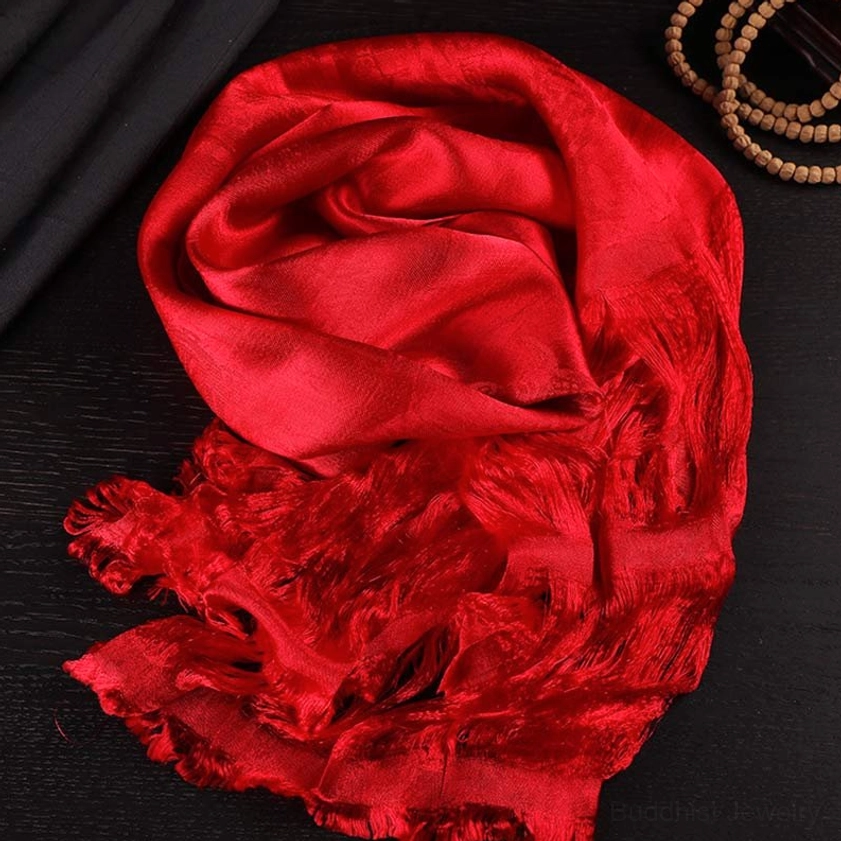 Deep red sacred Buddhist khata blessing scarf with draped rolled design on dark wooden table with prayer beads