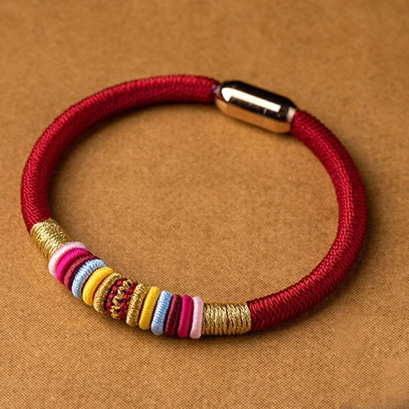 Red woven Buddhist protection bracelet with magnetic buckle and colorful bead accents overhead shot