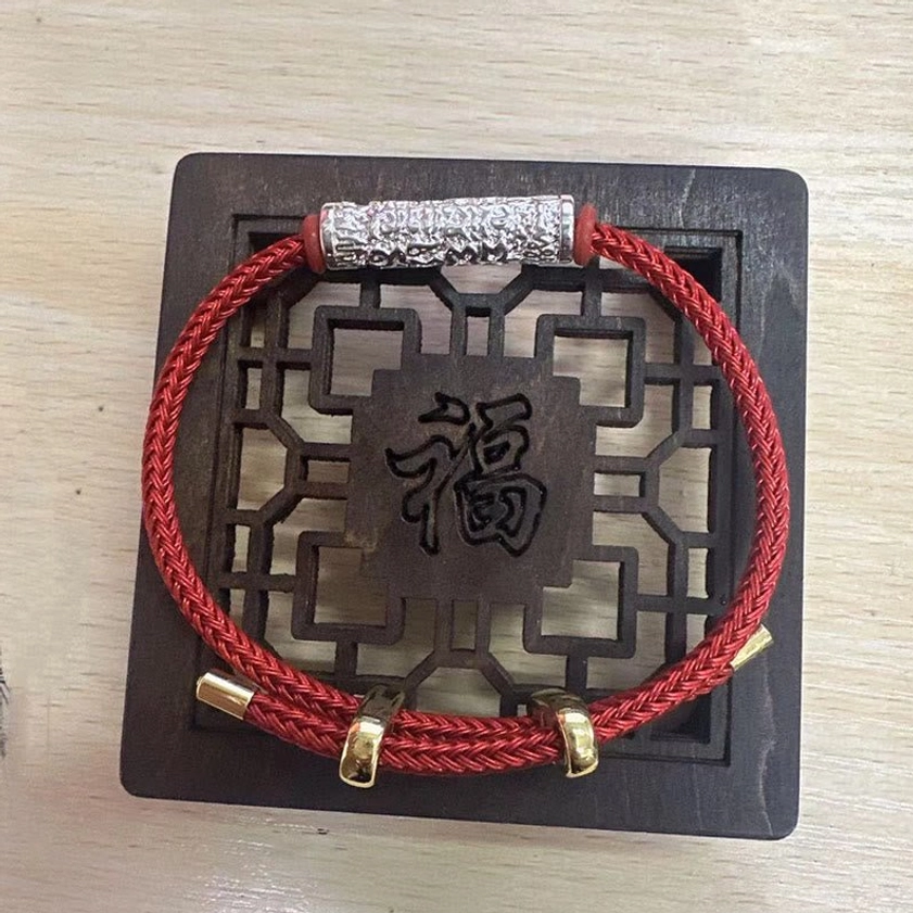 Red braided Buddhist protection bracelet with silver metal tube detail on blessed wooden tray