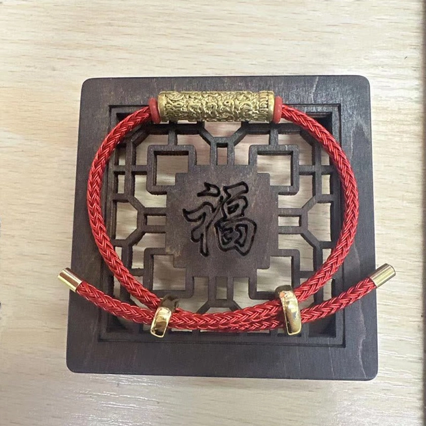 Red woven Buddhist string bracelet with gold engraved copper accent on traditional Chinese wooden tray