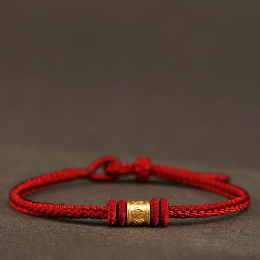 Red braided Buddhist string bracelet with gold Om Mani Padme Hum engraved bead, front view on dark background