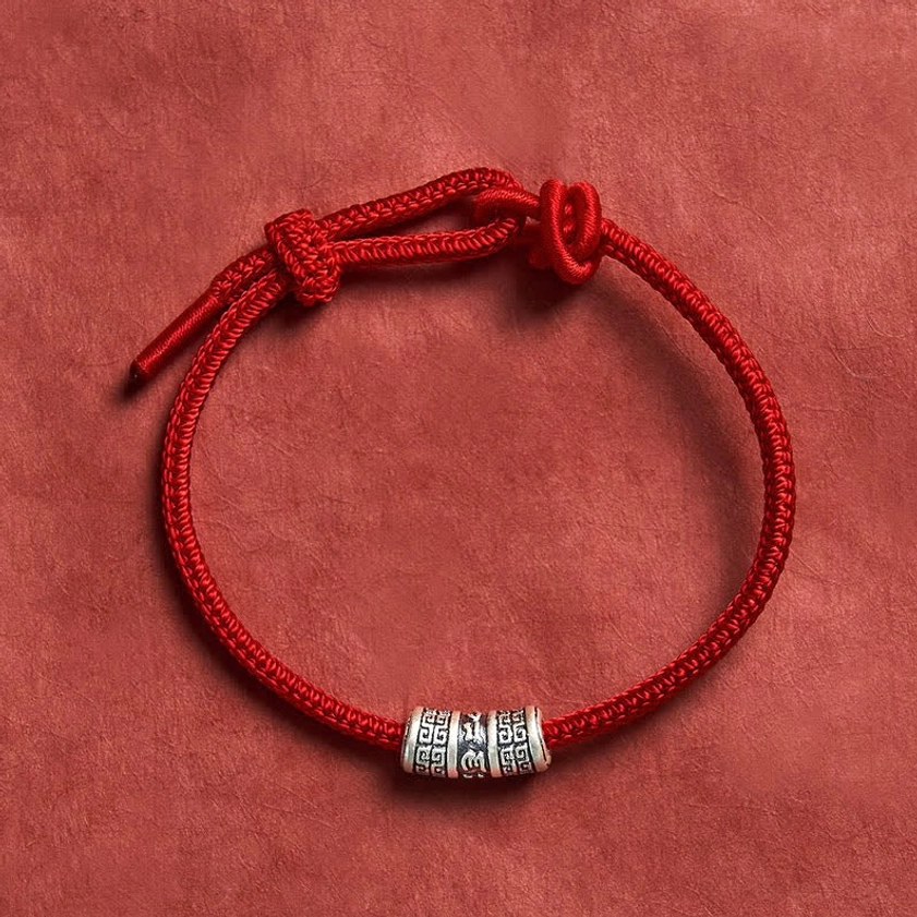 Red Buddhist string bracelet with silver Om Mani Padme Hum mantra bead, handmade braided cord, flat lay view on neutral backdrop