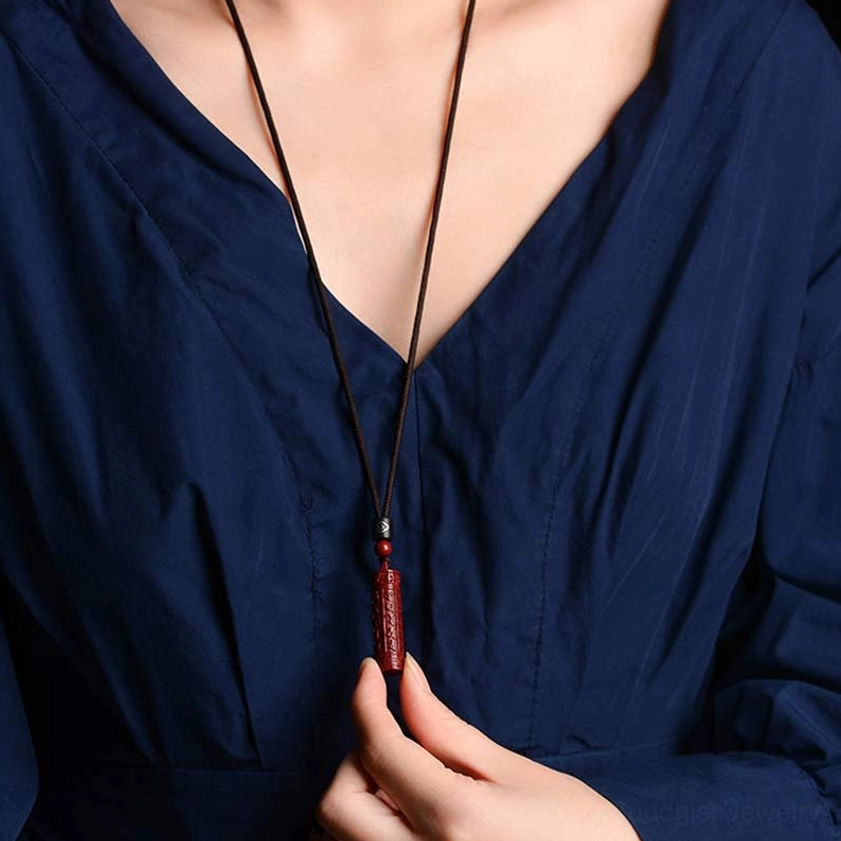 Cinnabar mantra cylinder pendant with smooth red polished body and engraved Buddhist patterns, displayed on wooden surface with bead accent