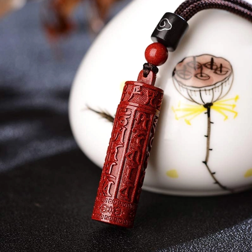 Cinnabar cylindrical mantra pendant with deep red color and engraved Buddhist scriptures, side profile showing carved details and traditional styling