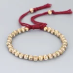 Red handmade copper bead Buddhist bracelet with adjustable tassel closure, front flat lay view