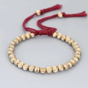 Red handmade copper bead Buddhist bracelet with adjustable tassel closure, front flat lay view