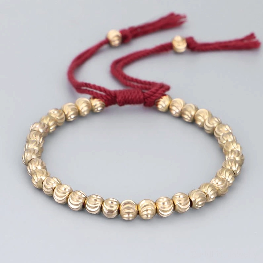 Red handmade copper bead Buddhist bracelet with adjustable tassel closure, front flat lay view