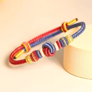 Red and dark blue eight-thread peace knot Buddhist bracelet with traditional braided cord displayed overhead on white background