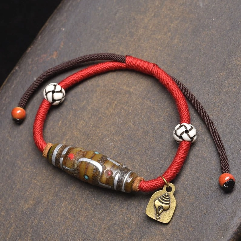 Red and brown braided rope nine-eye dzi bead protection bracelet with checkered beads and shell-shaped metal pendant overhead view