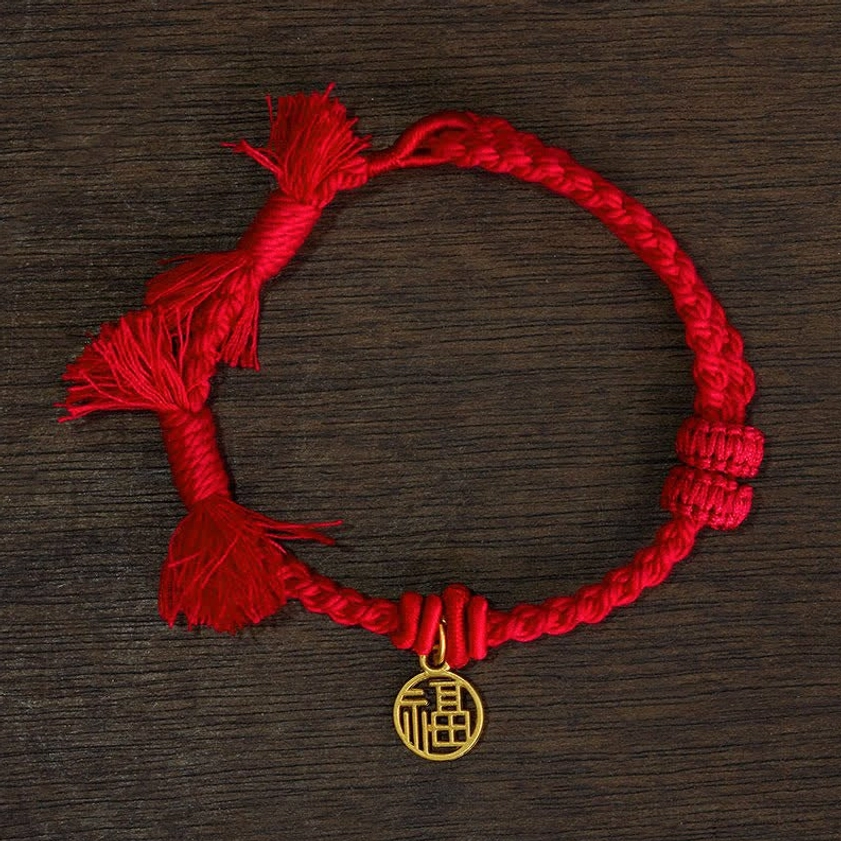 Red fu character string bracelet flat lay with gold fu charm on burgundy cord against wooden background