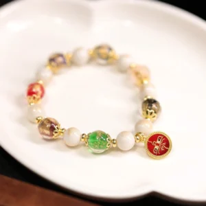 Red God of Wealth Buddhist charm bracelet with liuli glass beads and incense ash porcelain, displayed on white porcelain plate